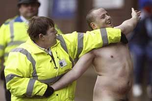 A Bury FC steward puts a streaker in a head lock after he ran on to the pitch during Saturday’s match